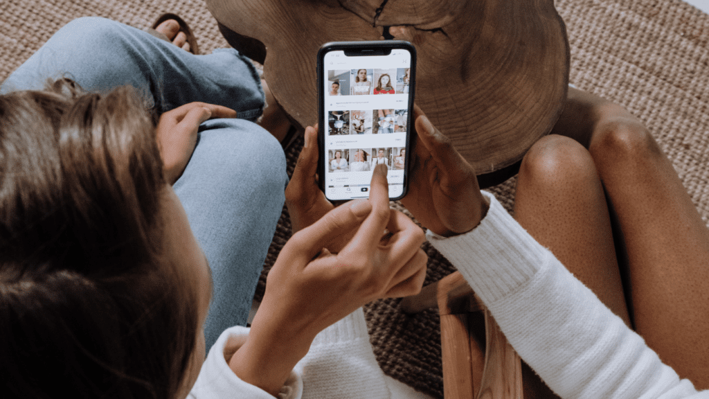 Two women are sitting on a floor connecting and contact with Safi Marketplace with a cell phone in their hands, contact us.