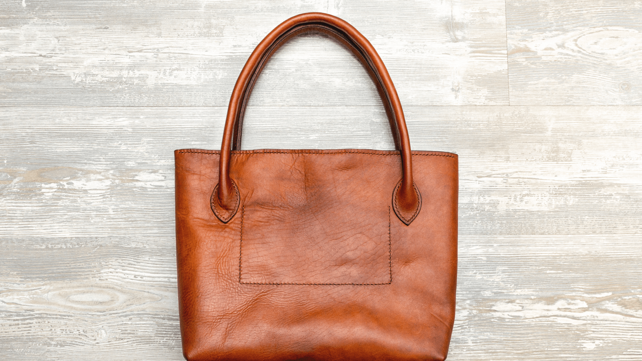 A brown leather tote bag on a wooden floor.